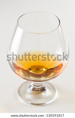 closeup of a brandy snifter on a white table top with a golden reflection to the side