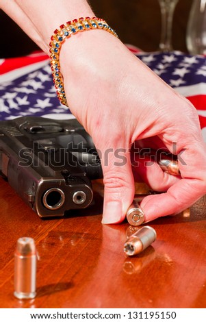 female hand grabbing a hallow point bullet with a gun and an american flag in the background