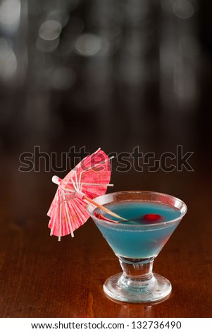 small tropical blue martini garnished with a cherry and a parasol