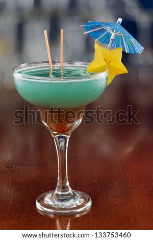 blue hawaiian cocktail served on a busy bar top garnished with a carambola slice and an umbrella