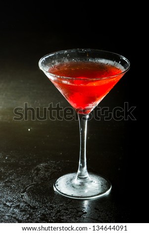 red cocktail on a dark background fading in to black garnished with a red cherry