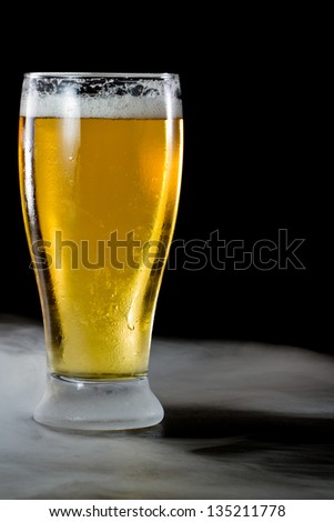 refreshing light beer in a cold glass served on a dark bar with fog
