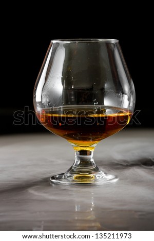 dramatic shot of a brandy snifter with whiskey served on a dark bar with fog around it