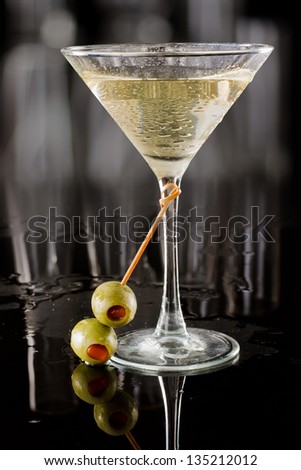 dirty vodka martini served on a dark bar garnished with large green olives