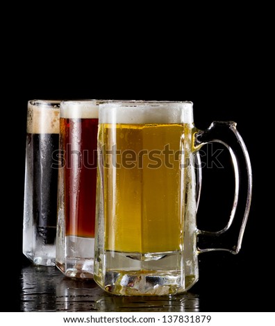 three frozen beer mugs isolated on a black background with different style beer in each one