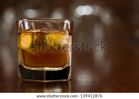 bourbon whiskey served with ice on a out of focus busy bar