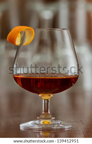 brandy snifter filled with an orange liquor served on a busy bar top garnished with an orange twist
