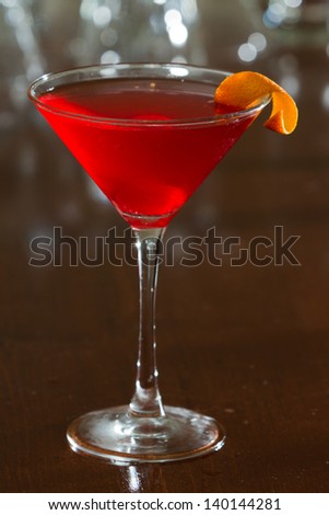 red cherry colored drink served up in a martini glass on a out of focus bar top
