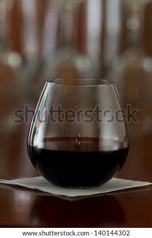stemless glass with red wine served on a busy out of focus bar