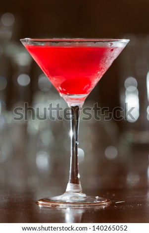 red cherry colored drink served up in a martini glass on a out of focus bar top