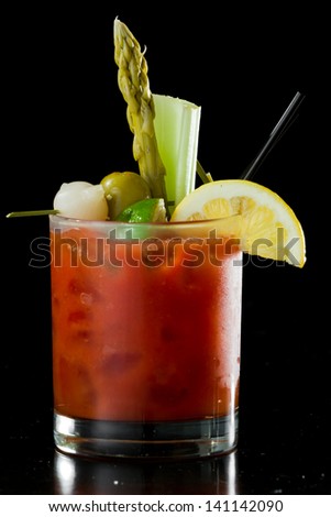 spicy Bloody Mary served on a dark bar garnished with pickled veggies and a lemon
