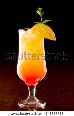 tequila sunrise, fresh orange juice with tequila and cherry juice served in a stem glass on a dark bar