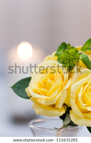 closeup of yellow roses as a centerpiece with a candle on the background