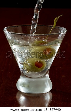 dirty vodka martini splashing into a cocktail glass with green olives