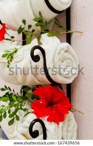 white rolled towels on a wall rack decorated with fresh red hibiscus flowers