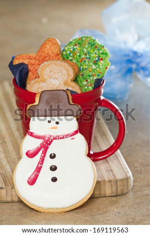 close up of holiday Christmas cookie in the shape of a snow man with a red coffee cup filled with cookies