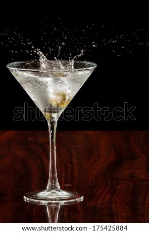 close up of  garlic stuffed martini olives splashing into a cocktail over a dark background