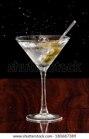 close up of  garlic stuffed martini olives splashing into a cocktail over a dark background