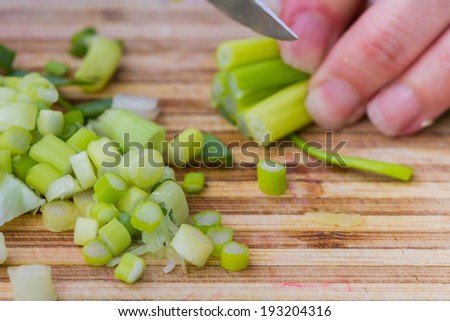 closeup of hand in motion slicing  fresh clean leeks or green onions on a cutting board