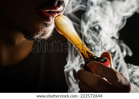 studio shoot with model simulating smoking pot with a pipe in a dark high contrast image