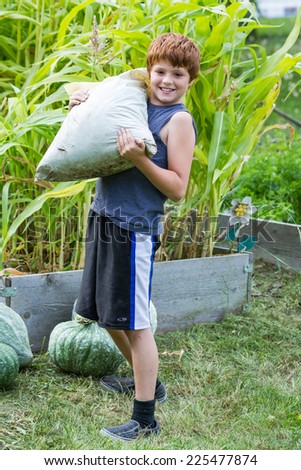 portrait of a young boy holding a large bag of mulch for the raised garden beds