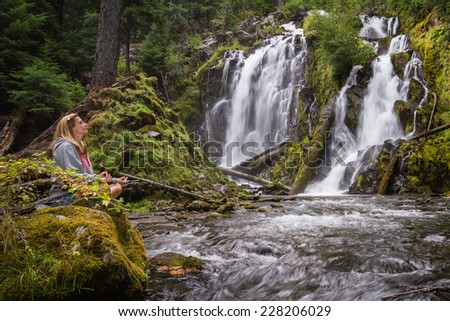 pretty woman relaxing and enjoying serene scene of national creek falls in Oregon