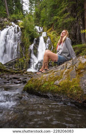 pretty woman relaxing and enjoying serene scene of national creek falls in Oregon