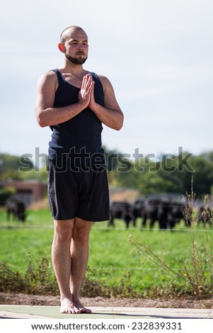 young caucasian man practicing outdoor yoga wearing a black tank top