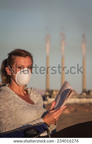 concept image of a woman sitting reading a book wearing a mask with a coal power plant and dirty smoke in the background