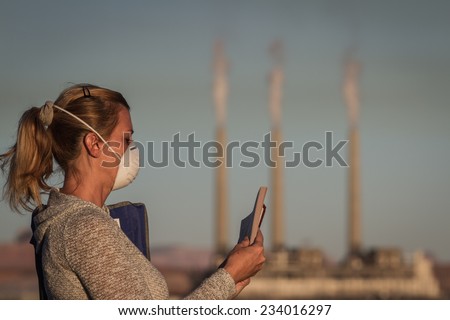 concept image of a woman sitting reading a book wearing a mask with a coal power plant and dirty smoke in the background