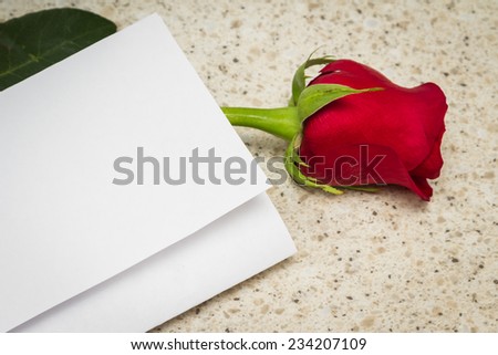 blank note and a single long stem red rose on a kitchen table of a love concept