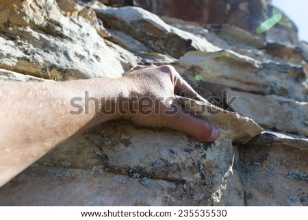 close up of a hand gripping a small shelf in the sandstone of a large cliff while rock climbing