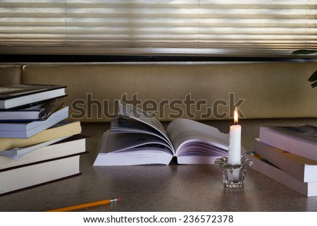 load of books on a candle light lit table with nobody studying