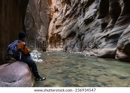 man hiking the Narrows in Zion National park with the virgin river flowing through the slot canyon