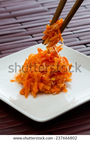 small serving of fermented carrots served on a small white plate with chop sticks