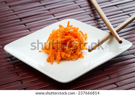 small serving of fermented carrots served on a small white plate with chop sticks