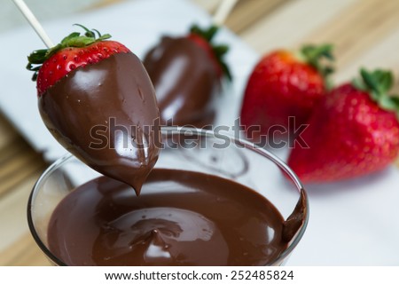 close up action shot of dipping fresh strawberries in dark chocolate at home