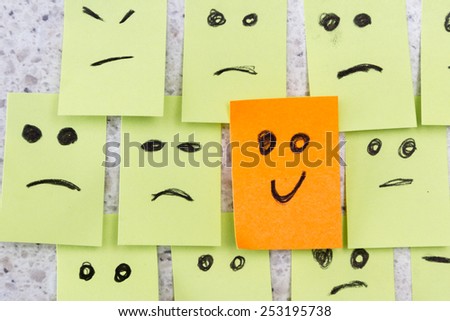 concept for a positive attitude with small office notes with multiple faces and one that stands out with a smile