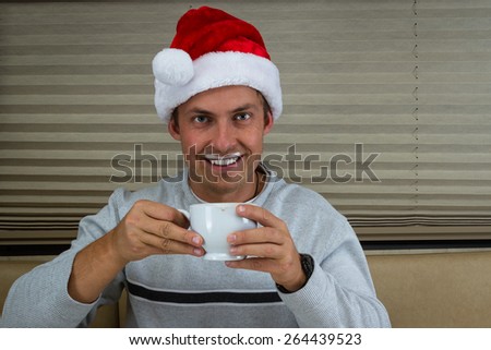 young man wearing a santa hat  drinking hot chocolate with foam on the upper lip