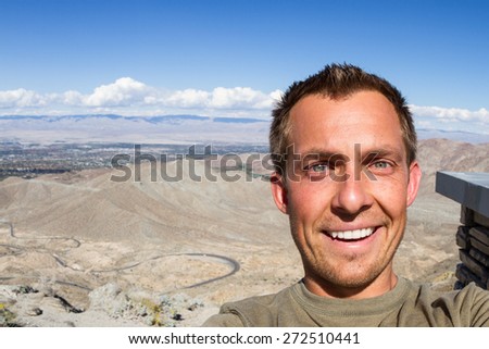 young man taking a selfie with the view of the desert valley in southern California