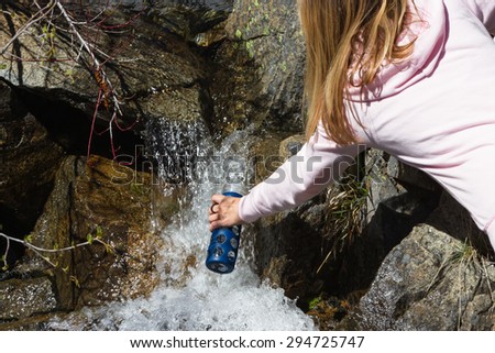 young woman filling her bottle with natural spring water flowing over rocks