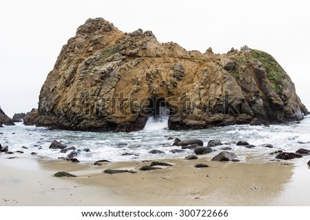 Large rock on the beach with a tunnel where the waves come in and out creating a natural feature and attraction