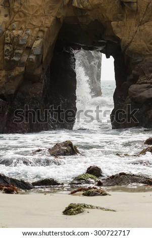 close up of a large rock with a natural tunnel and waves flowing thru it