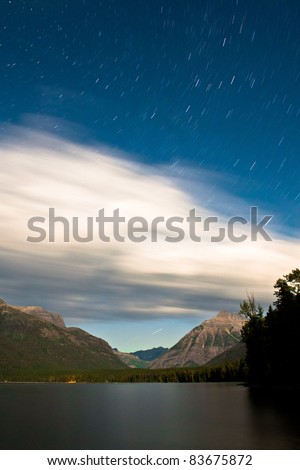 glacier national park in montana night sky with moon lit mountains and lake very long exposure