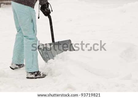 woman in snow suit shoveling and cleaning the driveway after a snow storm