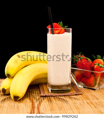 fresh strawberry banana banana milk shake on a tropical mat isolated on a black background