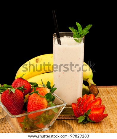 fresh strawberry banana banana milk shake on a tropical mat isolated on a black background