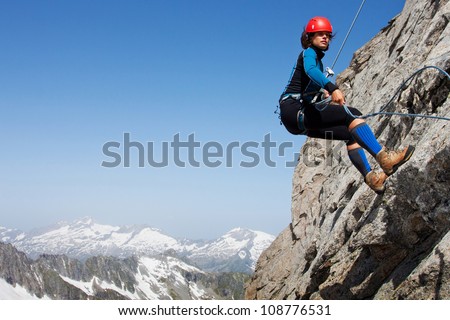 Young woman abseiling rock face in the Alps with large copy space