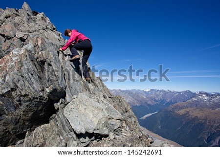 Young woman climbing rocky mountain ridge
