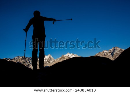 Silhouette of a man pointing with trekking pole towards mountain summit